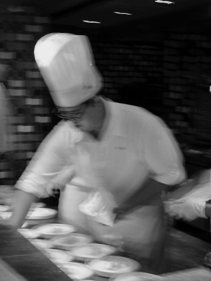 A chef in a traditional toque, focused on plating during a busy event.