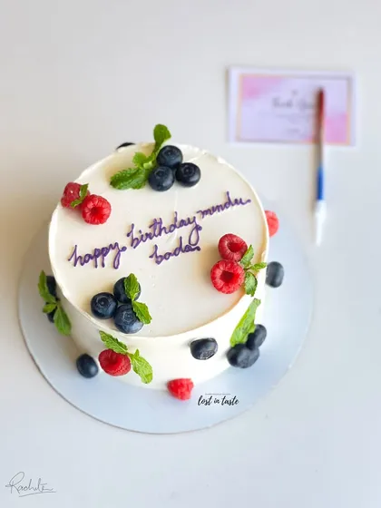 A simple yet beautiful celebration cake with chocolate buttercream, decorated with fresh raspberries, blueberries, and mint leaves for a pop of color and flavor.