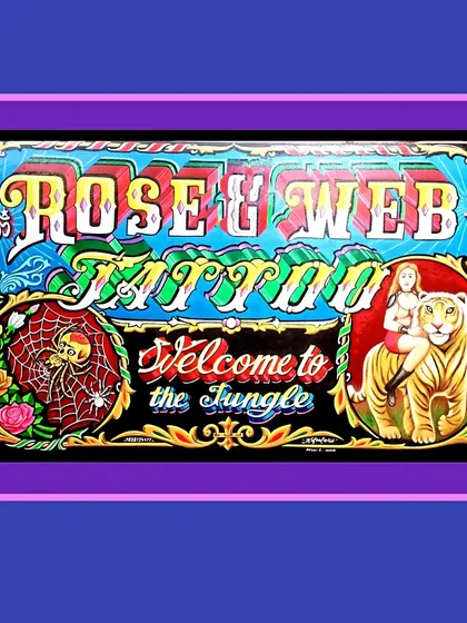 A sign for Rose & Web Tattoo in Ohio, USA. It features a spider in a web, a woman riding a tiger, and the phrase "Welcome to the Jungle."
