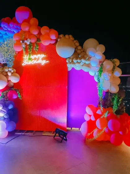 Another view of the vibrant rooftop party setup, showing the 'Happy Birthday' neon sign and the dramatic lighting against the night sky.