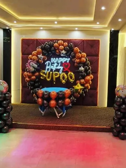 This birthday decoration was set up on a stage in a party hall. It features a balloon ring in black and copper tones, with a personalized neon sign and a central table for the cake.