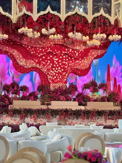 A view of the unique and surreal stage design. The massive red floral sculpture hangs like a cloud over the stage, set against a vibrant blue digital backdrop.