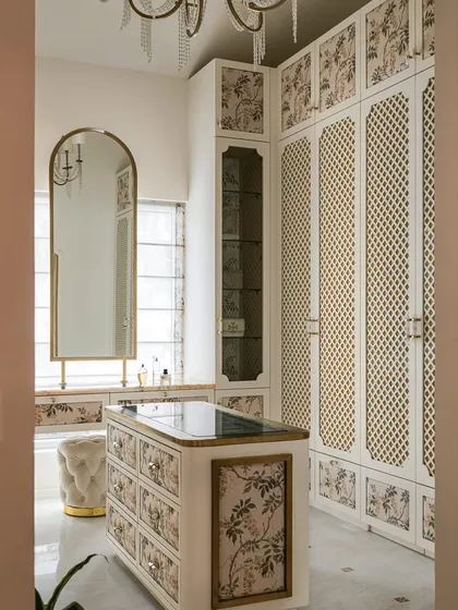 A walk-in closet should be a personal sanctuary. We designed this bespoke space with delicate floral panels, classic latticework shutters, and gilded accents to evoke old-world charm. The central island and tufted ottoman make it both functional and effortlessly luxurious.