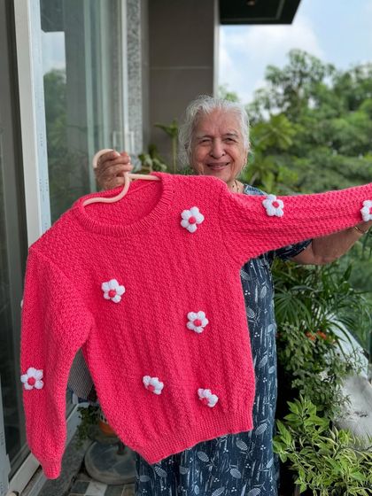 Simplicity with a touch of handmade charm. This lovely pink sweater is dotted with small, white crocheted flowers, adding a delicate and sweet detail to a classic design.