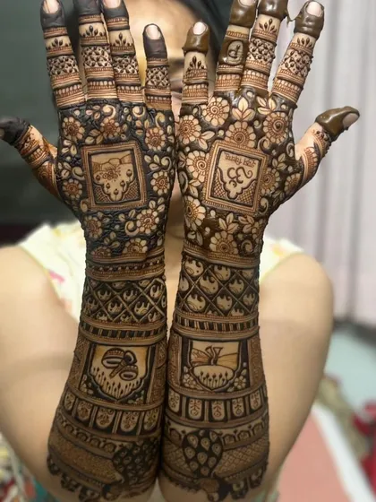 This intricate bridal design features various auspicious symbols in square panels. You can see a kalash, a swastika, and an 'Om' symbol, all woven into a beautiful pattern for blessings.