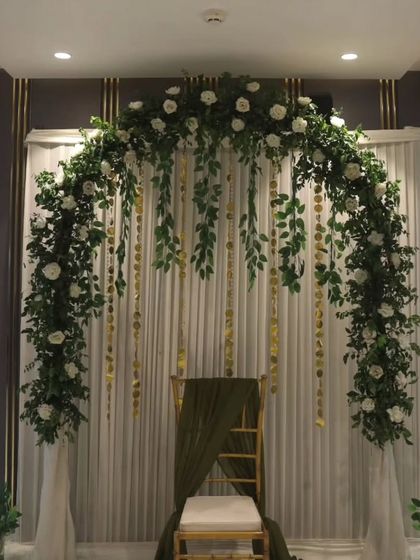 An elegant and fresh stage design with a green and white theme. The floral arch is made of white roses and lush greenery, with golden hanging elements that add a touch of sparkle.