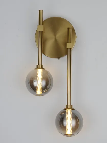 A modern wall sconce with two smoked glass globes on a brass fixture. A stylish choice for a bedroom or living area.