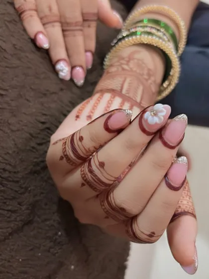 A close-up of the reverse French manicure for a bride. The design includes a subtle glitter base, a maroon border, and a single 3D flower accent on each hand.