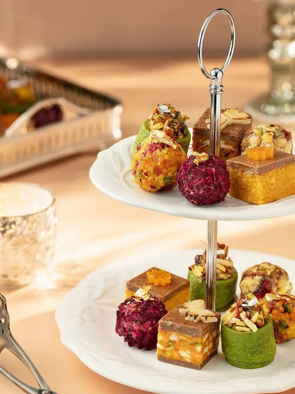 An assortment of modern Indian mithai elegantly displayed on a two-tiered stand. This image for Marriott Bonvoy showcases the variety and beauty of their Diwali collection, presented like a festive high tea.