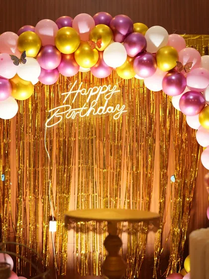 A close-up of the "Happy Birthday" neon sign against the gold shimmer backdrop from the butterfly theme. The small butterfly stickers on the balloons are a nice touch.