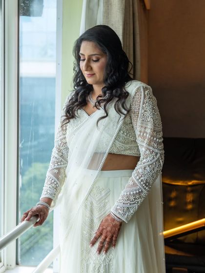 A contemplative moment by the window. The natural light highlights the soft waves in her hair and the flawless finish of her makeup.