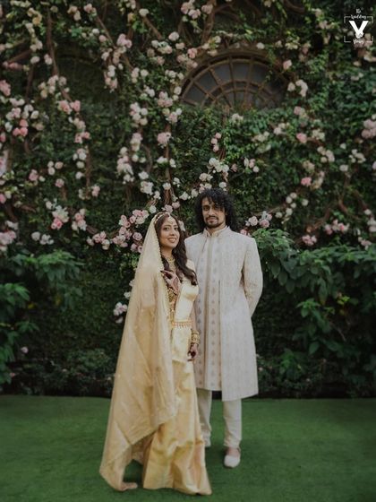 A classic portrait of the couple standing before a wall of beautiful pink and white flowers. The natural backdrop adds a touch of romance and elegance to their wedding photo.