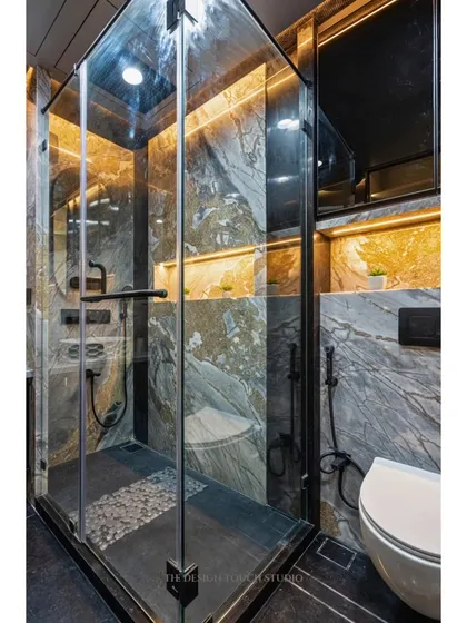 A compact yet luxurious bathroom design. The space features a glass-enclosed shower with matte black fixtures and beautiful marble walls with earthy golden and grey veins.