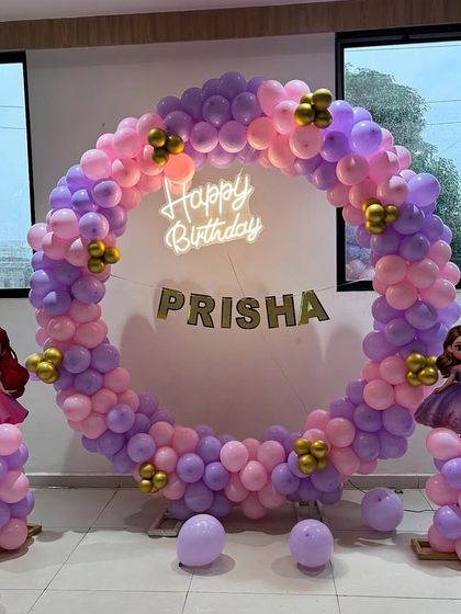 A princess-themed birthday party featuring a full circular balloon arch in pink and purple. The setup is flanked by balloon pillars with princess cutouts.