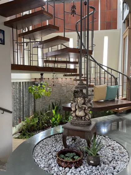 The entrance to a home should be an experience of tranquility. This foyer features a custom spiral staircase wrapping around an indoor courtyard, using natural elements like stone, water, and plants to welcome positivity and nature into the home.