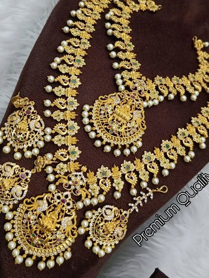 A premium quality South Indian temple jewellery set. It features carvings of deities, peacock motifs, and is adorned with pearls, perfect for a traditional bride.