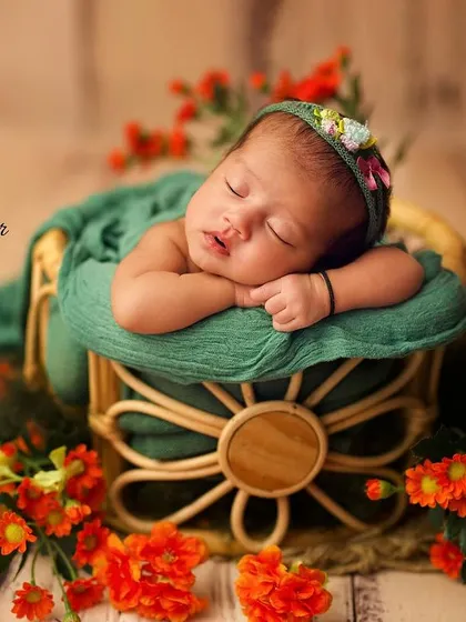 A newborn rests peacefully in a basket adorned with vibrant orange flowers, showcasing a bold and beautiful color theme.
