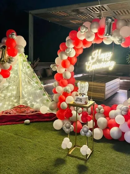 This is the full view of a beautiful first-anniversary terrace decoration. The setup includes a large balloon arch, a cozy light-up tent, and a cake stand, creating a complete party space.