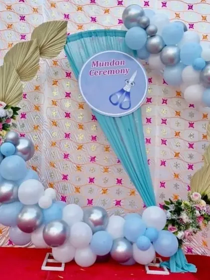 An elegant setup for a "Mundan Ceremony." This design uses a ring frame with blue draping, a custom sign, and a balloon garland in shades of blue, white, and silver, accented with dried palm leaves.