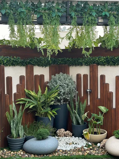 This compact garden design shows how to maximize small spaces. A wooden fence provides a warm backdrop for hanging plants and a collection of floor planters, creating a dense green corner.