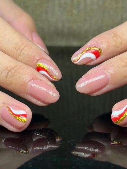 A festive design with red and white swirls topped with gold glitter on a sheer nude base.