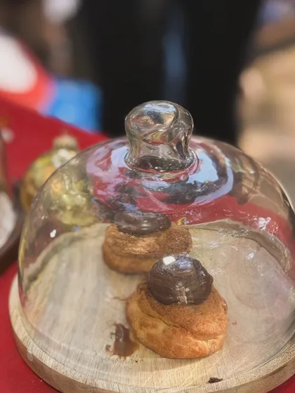 Chocolate choux pastries displayed under a glass cloche at my market stall. They are always one of the first things to sell out.