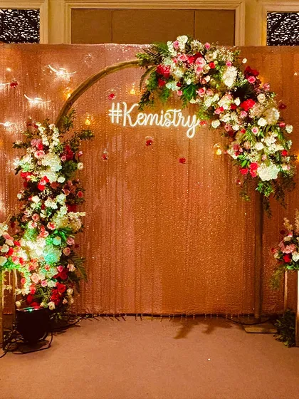 A chic photo backdrop for the "#Kemistry" wedding, featuring a glittering gold sequin wall and a romantic floral arch.