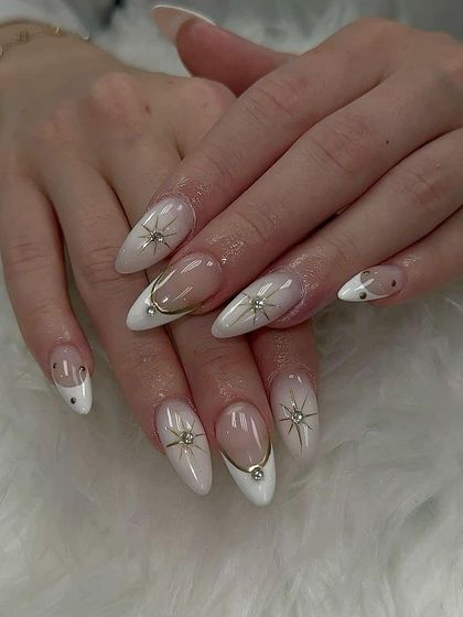 A celestial design on stiletto nails, featuring a white base with gold starbursts and rhinestone accents.