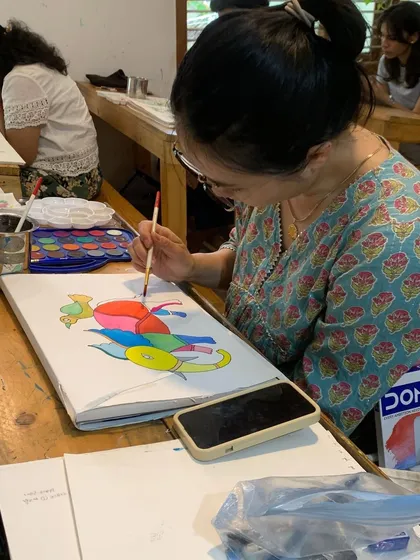 A student explores a vibrant folk art style, surrounded by the tools of her craft. Our classes offer a chance to dive into a wide variety of mediums, from pastels to traditional Indian arts.