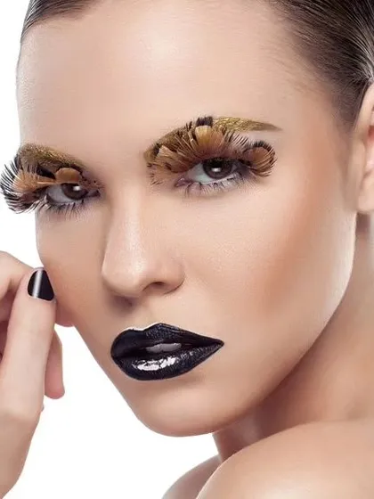 An avant-garde beauty shot featuring dramatic feather eyelashes and glossy black lipstick. This high-fashion makeup look is captured against a clean white background to emphasize the artistry.