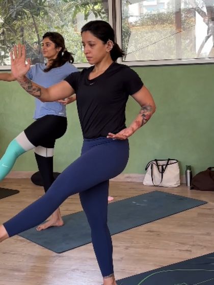 Two members practicing a balancing pose, demonstrating focus and strength. The tattoos show the diverse community we welcome.