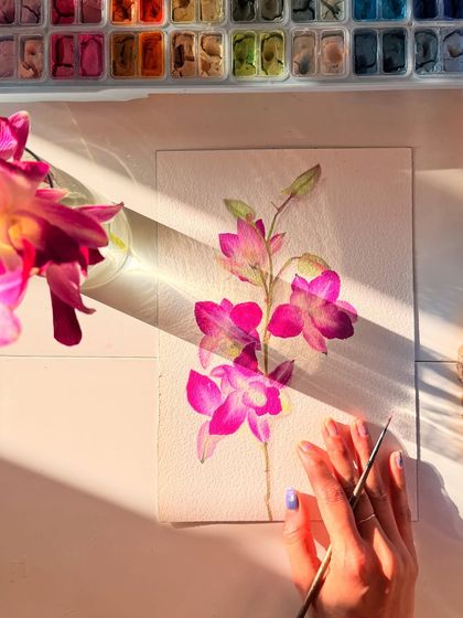 A close-up shot of me adding the final touches to my pink orchid painting. You can see my gouache palette and the careful brushwork required for these detailed botanical illustrations.