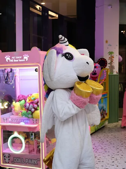 Our unicorn mascot ready to bring smiles and magic to a birthday party, standing next to our claw machine.