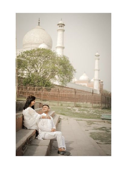 A timeless, classic shot of a couple sharing a quiet moment on the steps near the Taj Mahal, dressed in elegant white.