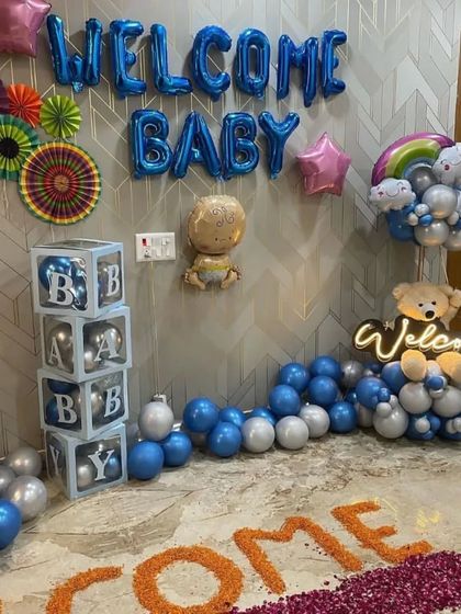 A detailed shot of the "Welcome Baby" setup, highlighting the "BABY" blocks, foil balloons, and neon "Welcome" sign with a teddy bear.