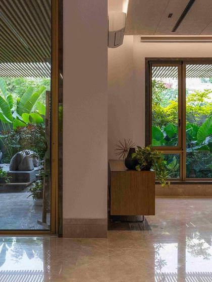 A seamless transition from a marble-floored interior to a verdant outdoor patio. The design uses large glass panels to dissolve the barrier between inside and out, making the garden a constant presence.