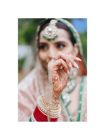 A detail shot focusing on a Sikh bride's hand, showing her ring and traditional red chooda.