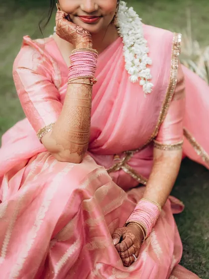 A close-up portrait of the bride, Dhriti, showcasing her beautiful pink saree, intricate henna, and the delicate gajra in her hair.