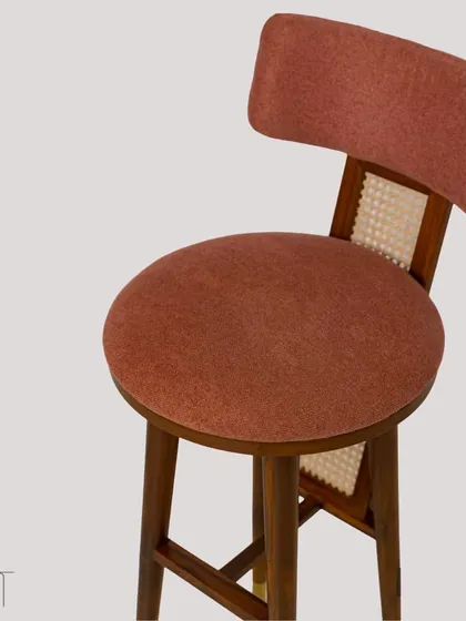 A detail of the 'Lithe Perch' bar chair, showing the comfortable upholstered seat and backrest with rattan detailing.
