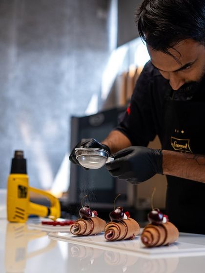 A chef dusting powdered sugar over chocolate curls. It's these finishing touches that create a truly professional-looking pastry.