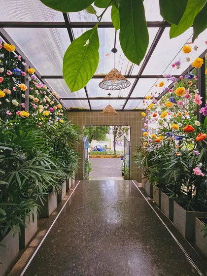 The entrance to a cafe, transformed into a floral wonderland for a baby shower. The pathway is lined with lush plants and hanging flowers, creating a secret garden feel.