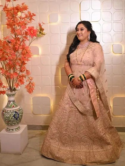 Another beautiful shot of the bride by the decorative wall. The soft lighting highlights the intricate details of her lehenga and her glowing makeup.
