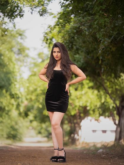 A full-length shot of a model in a black velvet dress, posed confidently on a path in the woods.