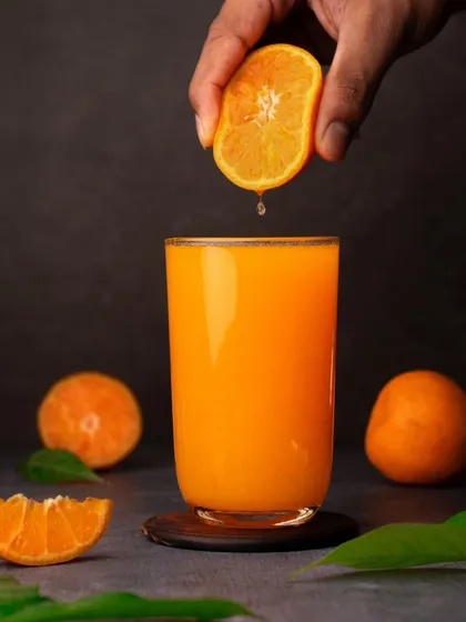 A dark and moody shot of a hand squeezing a fresh orange into a glass of juice. The dramatic lighting makes the simple act look artistic.