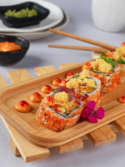 Beautifully crafted sushi rolls on a bamboo platter. The pops of orange and red from the roe and sauce, combined with the edible flower garnish, make this a true visual treat.