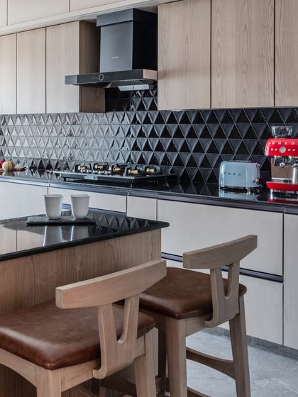 This open kitchen, with its beautiful breakfast table, is the heart of this Mumbai home. I designed it to be perfect for creating memories, with black triangular tiles, warm wood, and a pop of red from the coffee machine.
