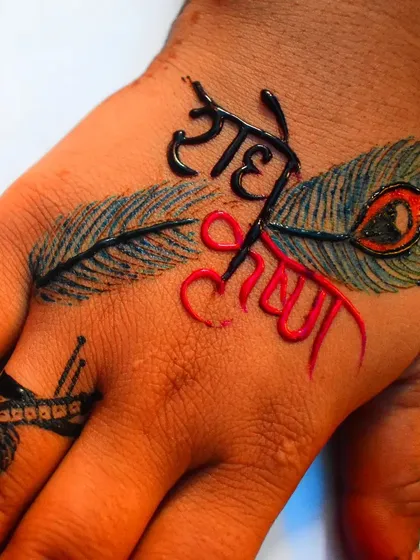 This is a modern take on the classic Radhe Krishna theme, using colored henna to highlight the names. The design is placed on the back of the hand, accented with peacock feathers for a unique look.