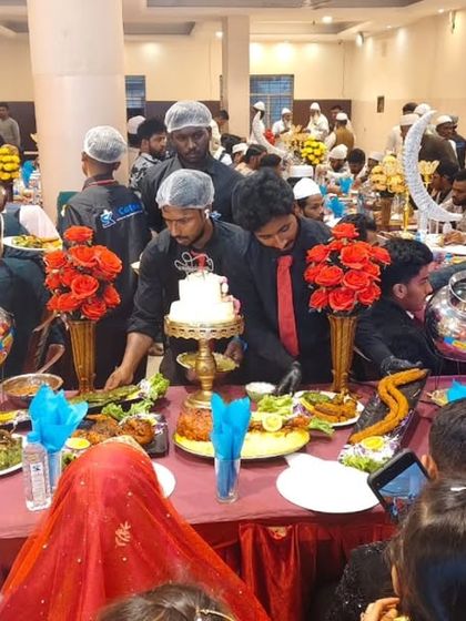 Our team carefully places the final touches, including a cake, on the 'Nousho ka Table' for a wedding celebration. The table is decorated with swan-like centerpieces and red roses.