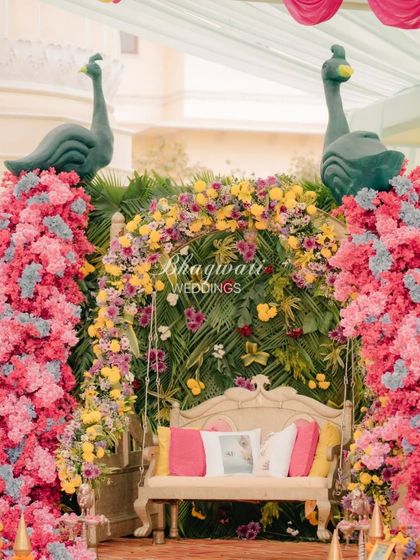 A beautiful seating area for the bride, flanked by two floral peacock installations. The swing is set against a lush green backdrop, creating a picturesque spot for the haldi ceremony.