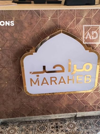 The reception desk of 'Maraheb' restaurant, featuring a custom wallpaper with a geometric fan pattern. The wallpaper complements the custom signage and patterned floor tiles.
